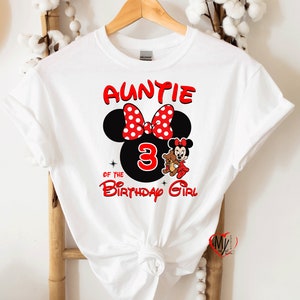 May include: White t-shirt with red text that says "Auntie of the Birthday Girl" with a black and red Minnie Mouse head and a number 3.  Minnie Mouse is holding a brown teddy bear.
