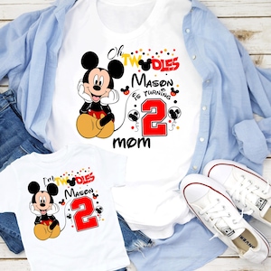 May include: White t-shirts with a Mickey Mouse graphic and the text "Oh Twodles Mason is turning 2 mom" and "I'm Twodles Mason 2". The shirts are paired with blue jeans, a light blue button-down shirt, and white sneakers.