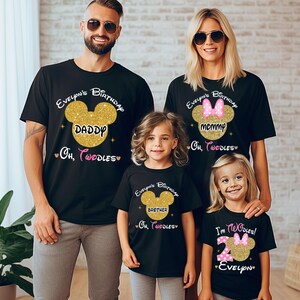 Puede incluir: Una familia de cuatro personas con camisetas negras con orejas de Mickey Mouse de purpurina dorada y texto que dice "Evelyn's Birthday", "Daddy", "Mommy", "Brother", "Oh, Toodles", y "I'm Toodles! Evelyn".