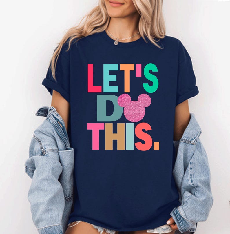 May include: Navy blue t-shirt with the text "LET'S DO THIS" in colorful block letters and a glittery pink Mickey Mouse head. The shirt is a casual style, suitable for everyday wear.