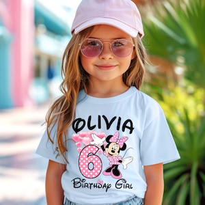 Puede incluir: Una camiseta azul claro con el nombre "Olivia" en negro, el n&uacute;mero rosa "6" con lunares blancos y un dise&ntilde;o de Minnie Mouse. Las palabras "Birthday Girl" est&aacute;n debajo.