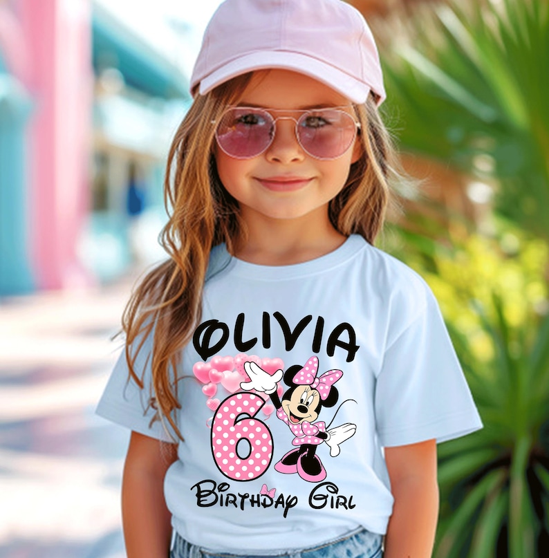 Puede incluir: Una camiseta azul claro con el nombre "Olivia" en negro, el n&uacute;mero rosa "6" con lunares blancos y un dise&ntilde;o de Minnie Mouse. Las palabras "Birthday Girl" est&aacute;n debajo.