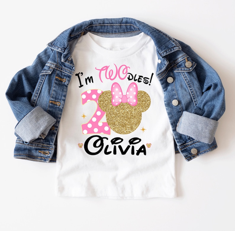 Puede incluir: Camiseta blanca con un dise&ntilde;o de Minnie Mouse rosa y dorado. La camiseta dice "I'm Two-dles!" y "Olivia" en texto negro.