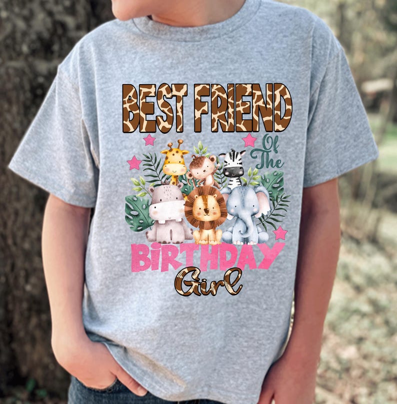 May include: A heather gray t-shirt featuring a graphic of a giraffe, monkey, zebra, hippo, lion, and elephant surrounded by green leaves and pink stars. The text reads BEST FRIEND Of The BIRTHDAY Girl in brown and pink lettering.