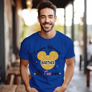 Puede incluir: Una camiseta azul real con una cabeza de Mickey Mouse de purpurina dorada y el texto "Evelynn's Birthday Brother Oh Toodles" impreso en la parte delantera.