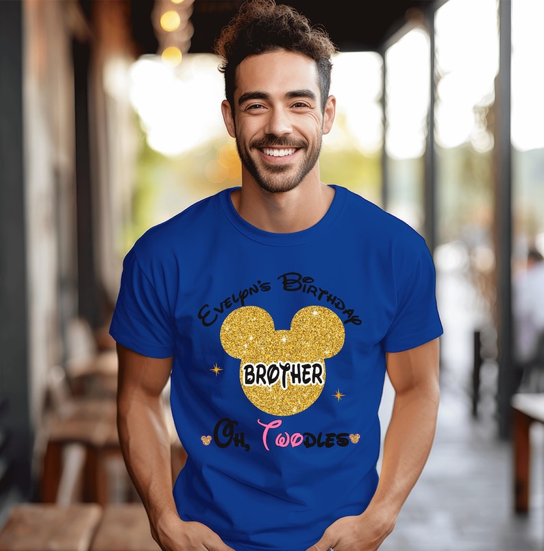 Puede incluir: Una camiseta azul real con una cabeza de Mickey Mouse de purpurina dorada y el texto "Evelynn's Birthday Brother Oh Toodles" impreso en la parte delantera.