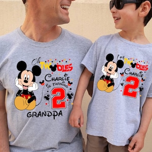 May include: Two gray t-shirts with Mickey Mouse graphics. One shirt says "Oh TWO-dles Charlie is turning 2 Grandpa" and the other says "I'm TWO-dles Charlie is turning 2". Both shirts feature a red number 2.