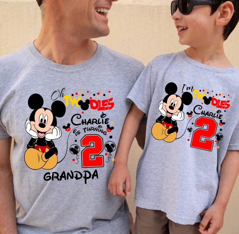 May include: Two gray t-shirts with Mickey Mouse graphics. One shirt says "Oh TWO-dles Charlie is turning 2 Grandpa" and the other says "I'm TWO-dles Charlie is turning 2". Both shirts feature a red number 2.