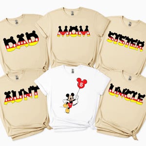 May include: A selection of beige and white t-shirts with Mickey Mouse designs. The shirts display the words "DAD", "MOM", "SISTER", "AUNT", and "UNCLE" in a black, red, yellow, and white font. One shirt features a Mickey Mouse graphic holding a balloon.