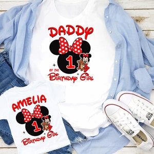 May include: Two white t-shirts featuring a red and black Mickey Mouse design. The larger shirt reads "Daddy of the Birthday Girl" with the number 1. The smaller shirt reads "Amelia 1 Birthday Girl".