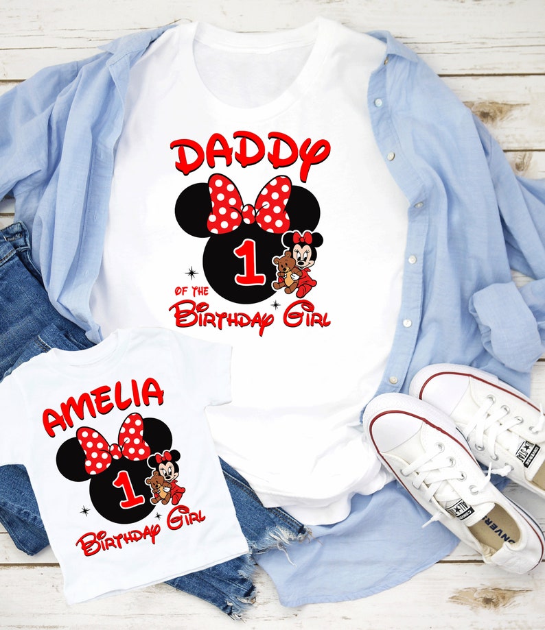 May include: Two white t-shirts featuring a red and black Mickey Mouse design. The larger shirt reads "Daddy of the Birthday Girl" with the number 1. The smaller shirt reads "Amelia 1 Birthday Girl".