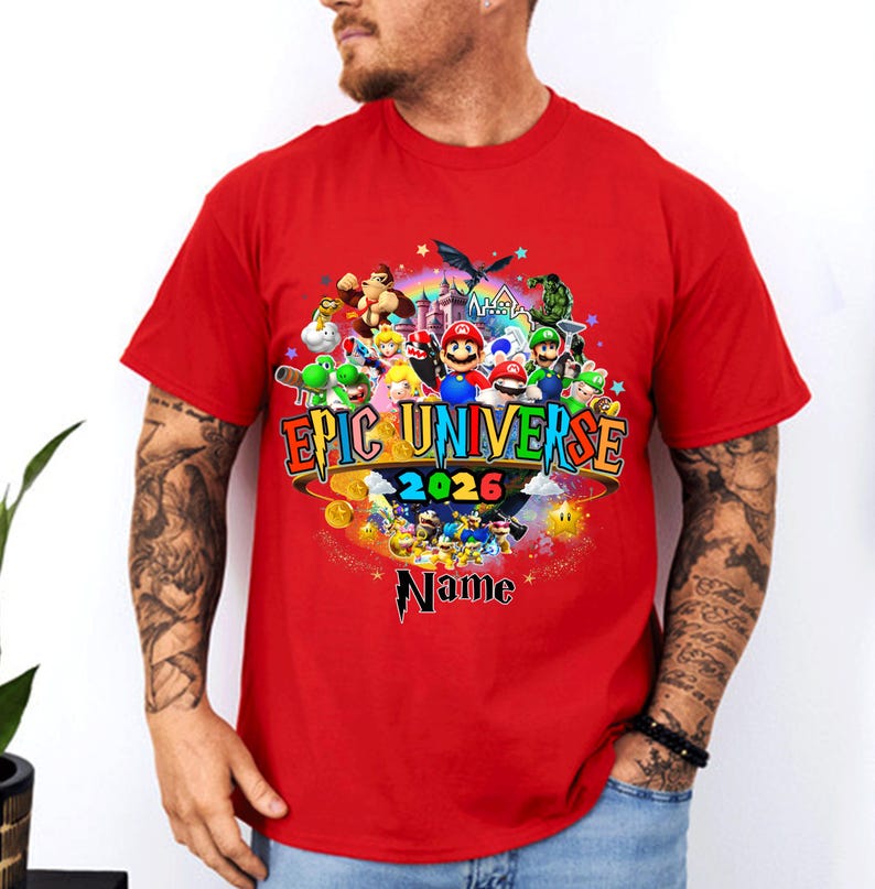 Pu&ograve; includere: T-shirt rossa con una grafica colorata. Il design include il testo "EPIC UNIVERSE 2026" e vari personaggi dei cartoni animati. La parola "Name" &egrave; sotto il testo principale, con stelle e un castello.