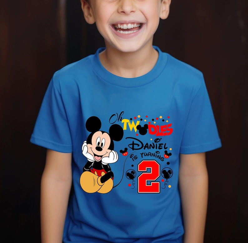 May include: A blue t-shirt featuring Mickey Mouse and the text "Oh TWO-DIES Daniel is turning 2". Mickey Mouse is in a seated position with his hands under his chin. The number 2 is in red with black balloons.