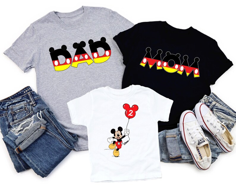 May include: Three t-shirts with graphic designs. A grey t-shirt with the word "DAD" in black, yellow, and red. A black t-shirt with the word "MOM" in black, yellow, and red. A white t-shirt with a Mickey Mouse graphic holding a red balloon.