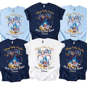 May include: A collection of six short-sleeved t-shirts in various colors: light blue, navy blue, and white. Each shirt features a colorful graphic with the text "Disney Family Vacation 2026" and a castle design with Disney characters. The phrase "Where the Magic Begins!" is also included.