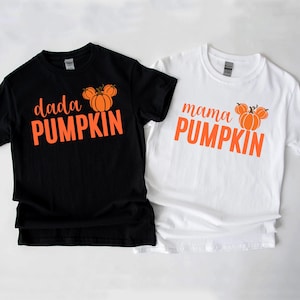 Peut inclure: Deux t-shirts, un noir et un blanc, avec du texte orange et des graphiques de citrouilles. Le t-shirt noir indique "dada PUMPKIN", et le t-shirt blanc dit "mama PUMPKIN". Les deux sont à manches courtes.