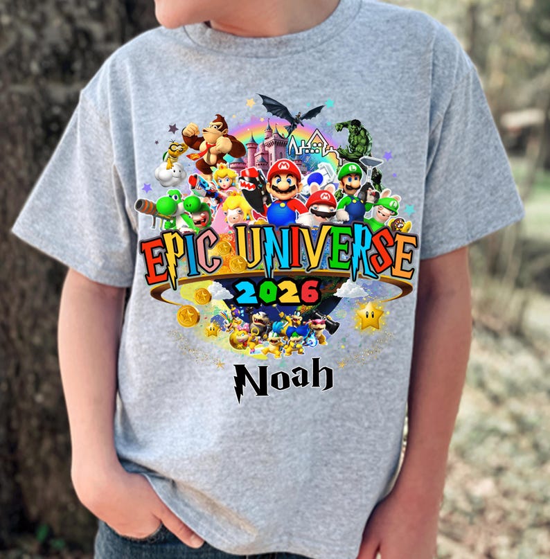 Pu&ograve; includere: Maglietta grigia con una grafica colorata. La grafica include il testo "Epic Universe 2026" e il nome "Noah", insieme a vari personaggi dei cartoni animati e un arcobaleno.
