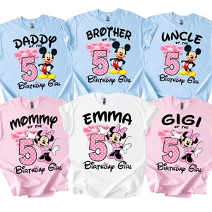 Puede incluir: Seis camisetas coloridas con dise&ntilde;os de cumplea&ntilde;os. Las camisetas son de color azul claro, rosa y blanco. Cada camiseta presenta el n&uacute;mero 5, un gr&aacute;fico de Mickey o Minnie Mouse y textos como "Daddy", "Mommy", "Emma", "Brother", "Uncle" y "Gigi".