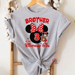 May include: Grey t-shirt featuring a red and white Minnie Mouse head design. The design includes the text "Brother of the 3 Birthday Girl".