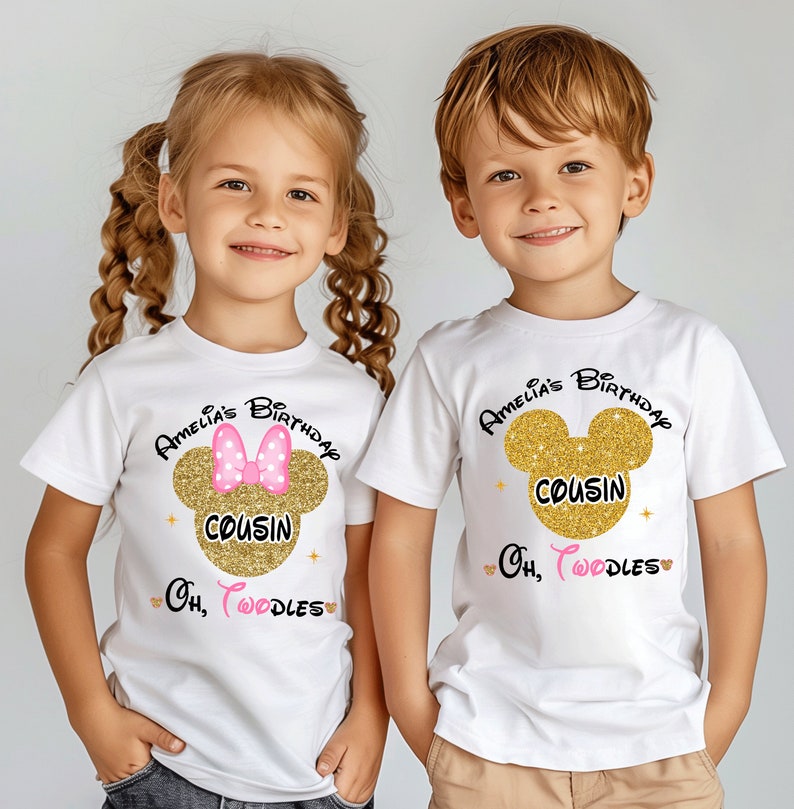 Puede incluir: Dos camisetas blancas con orejas de Mickey Mouse de purpurina dorada y el texto "Amelia's Birthday Cousin Oh, Toodles". La camiseta de la ni&ntilde;a tiene un lazo rosa en las orejas de Mickey Mouse.