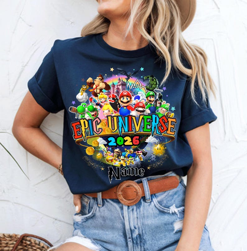 Pu&ograve; includere: T-shirt blu navy con una grafica colorata di personaggi di videogiochi, tra cui Mario e Luigi. Il testo "EPIC UNIVERSE 2026" &egrave; ben visibile. &Egrave; incluso anche un nome personalizzato.