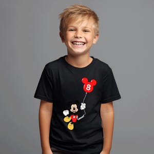 May include: Black t-shirt with a Mickey Mouse design holding a red balloon shaped like Mickey's head, with the number 8. The name "Samuel" is written on the string. The shirt is worn by a smiling child.