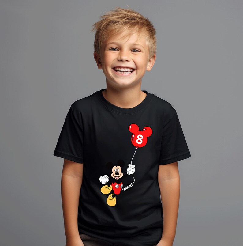 May include: Black t-shirt with a Mickey Mouse design holding a red balloon shaped like Mickey's head, with the number 8. The name "Samuel" is written on the string. The shirt is worn by a smiling child.