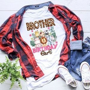 May include: A white t-shirt featuring a graphic print with the text BROTHER of The BIRTHDAY Girl in brown giraffe-patterned and pink lettering. The design includes watercolor illustrations of a giraffe, monkey, zebra, hippo, lion, and elephant.
