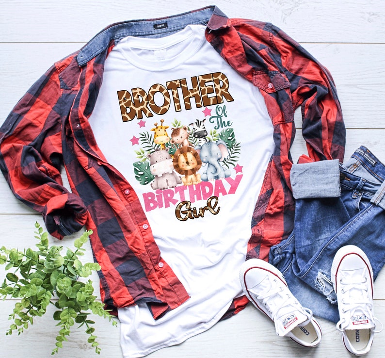 May include: A white t-shirt featuring a graphic print with the text BROTHER of The BIRTHDAY Girl in brown giraffe-patterned and pink lettering. The design includes watercolor illustrations of a giraffe, monkey, zebra, hippo, lion, and elephant.
