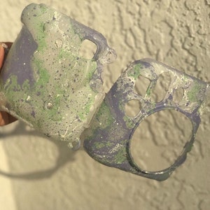 Peut inclure: Un étui pour appareil photo en deux parties avec un motif de peinture éclaboussée dans des tons de vert, de violet et de blanc.
