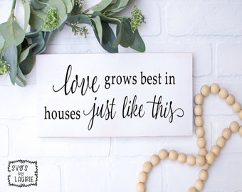 May include: White wooden sign with black calligraphy that reads "Love grows best in houses just like this".