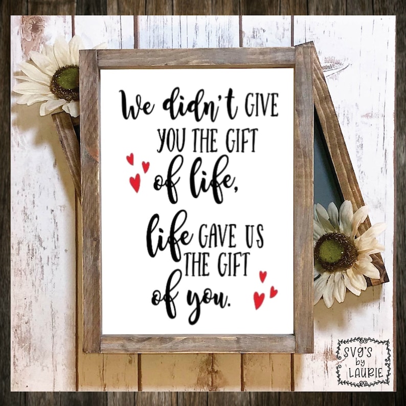May include: A white wooden sign with black text that reads "We didn't give you the gift of life, life gave us the gift of you." There are small red hearts scattered around the text.