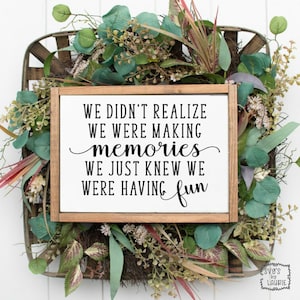 Puede incluir: Un letrero de madera con el texto "We didn't realize we were making memories we just knew we were having fun". El letrero está rodeado de vegetación.