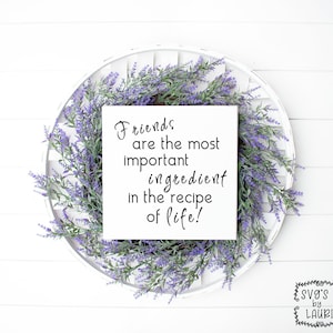 Może przedstawiać: Biały kwadratowy znak z czarnym tekstem, który brzmi: "Friends are the most important ingredient in the recipe of life!" Znak jest otoczony wieńcem fioletowych kwiatów.
