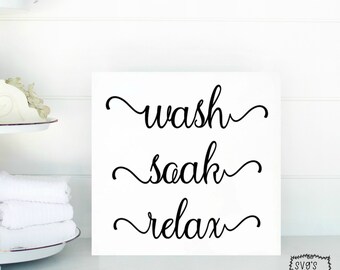 Może przedstawiać: Biały znak z czarnym tekstem pisanym kursywą, który brzmi "wash, soak, relax".