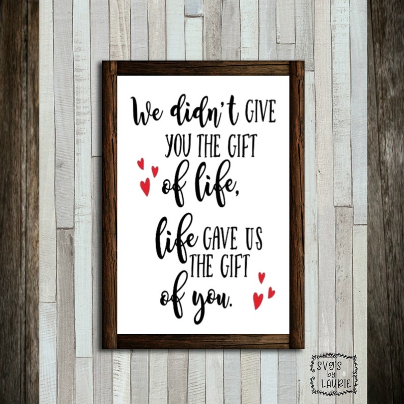 May include: A white sign with a black wooden frame and red hearts. The sign reads "We didn't give you the gift of life. Life gave us the gift of you."