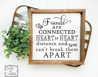May include: A white wooden sign with the text "Friends are CONNECTED HEART to HEART distance and time can't break them APART". The sign is in a brown wooden frame and is sitting on a white surface.