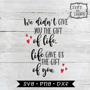 May include: Black and white text on a woodgrain background with red hearts. The text reads "We didn't give you the gift of life, life gave us the gift of you."