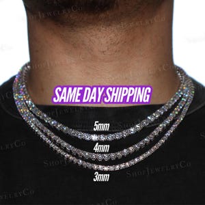 May include: Three silver-toned tennis necklaces featuring round-cut clear stones, displayed in varying widths of 3mm, 4mm, and 5mm. The necklaces are arranged in a layered style around the neck, showcasing a reflective, metallic finish and clear stones.