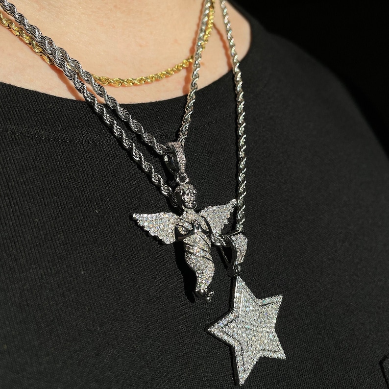 May include: A collection of silver-toned necklaces with diamond-like pendants. One necklace features an angel pendant, and another has a star pendant. The necklaces are layered with a gold-toned chain.
