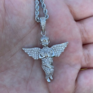 May include: Silver-toned angel pendant necklace with a detailed design. The angel has outstretched wings and is adorned with small, sparkling stones. The necklace chain is a matching silver color.