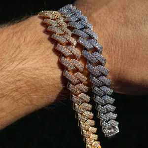 May include: Two gold and silver Cuban link chains with diamond accents. The chains are layered on a person's wrist.