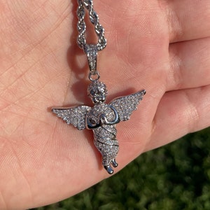 May include: Silver angel pendant necklace with a detailed design. The angel is covered in small, sparkling stones, with outstretched wings and clasped hands. The necklace has a rope chain.