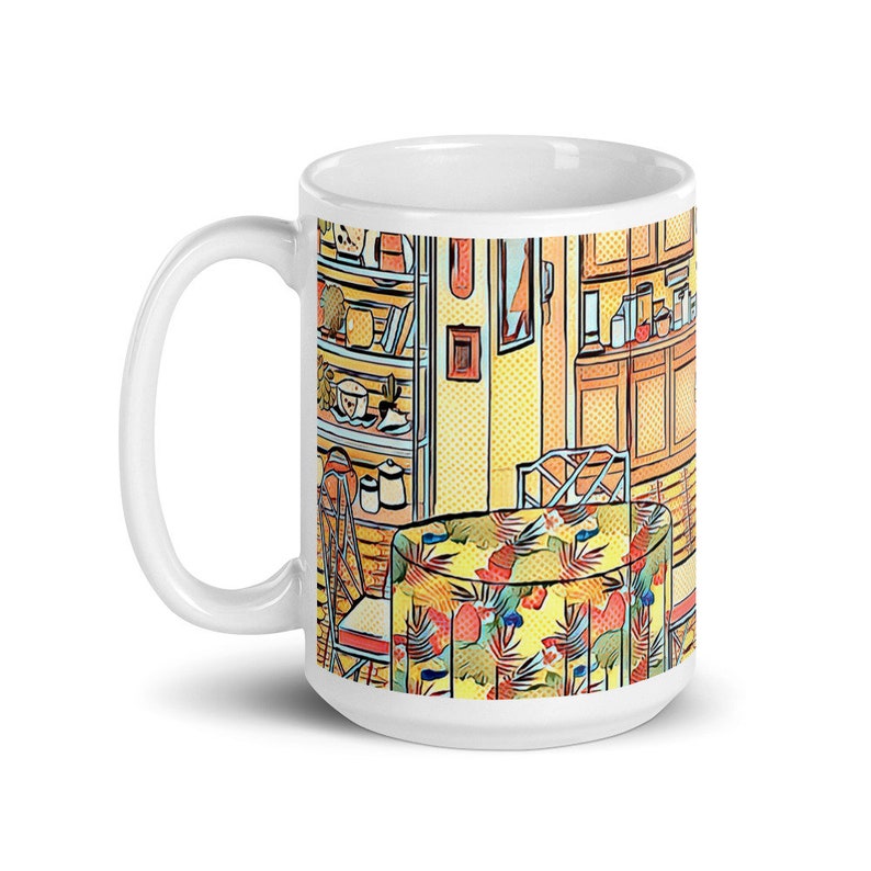 May include: White ceramic mug with a colorful illustration of a kitchen interior. The illustration features a table with a tropical print tablecloth, a chair, and a bookshelf filled with various items.