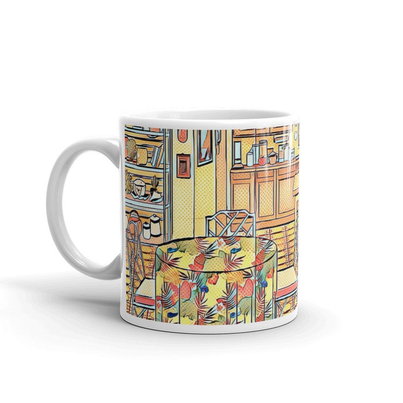 May include: A white ceramic mug with a colorful illustration of a kitchen interior. The illustration features a table with a floral tablecloth, chairs, and a cabinet with shelves filled with dishes and glasses.