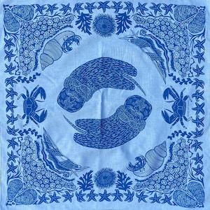 May include: A blue bandana with a white background featuring a repeating pattern of sea otters, crabs, starfish, and sea shells. The bandana has a blue border.