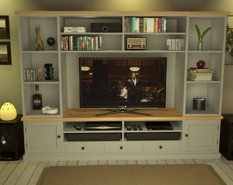 May include: A gray entertainment center with a large TV, shelves filled with books, CDs, and decorative items. A guitar, lamp, and speakers are also present, creating a cozy living room setting.
