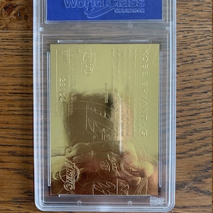 May include: A gold-colored Kobe Bryant basketball card with a picture of him in a Los Angeles Lakers uniform. The card is graded by World Class Grading and has a grade of 9.5.