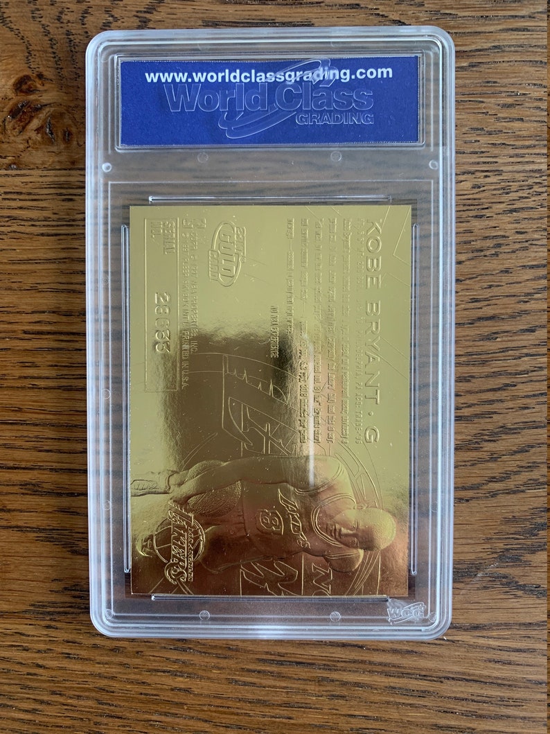 May include: A gold-colored Kobe Bryant basketball card with a picture of him in a Los Angeles Lakers uniform. The card is graded by World Class Grading and has a grade of 9.5.