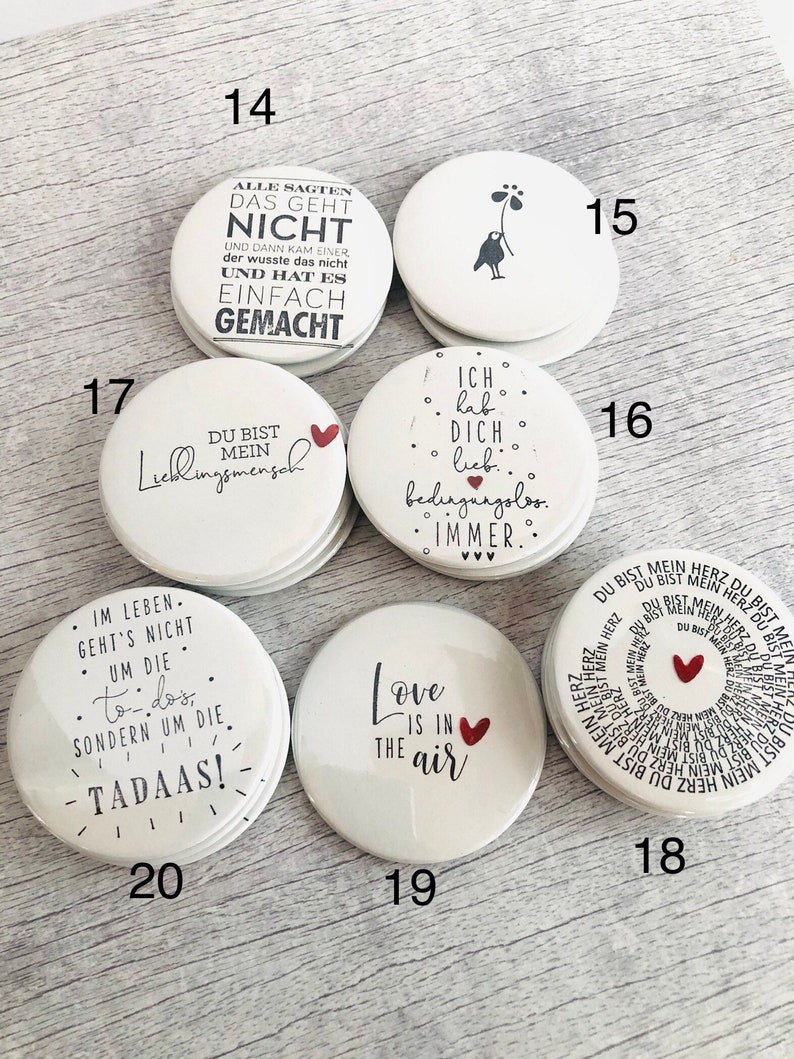 May include: A collection of white, round magnets with various black text and red heart designs. One magnet reads "Love is in the air." Another says "You are my favorite person."